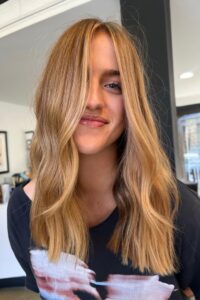 Dimensional golden copper blonde hair color with curtain bangs by Alyssa Black