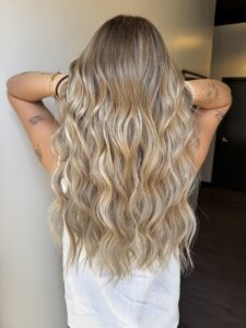 Long blonde balayage hair with a soft shadow root and beach waves by Brooke Bennett